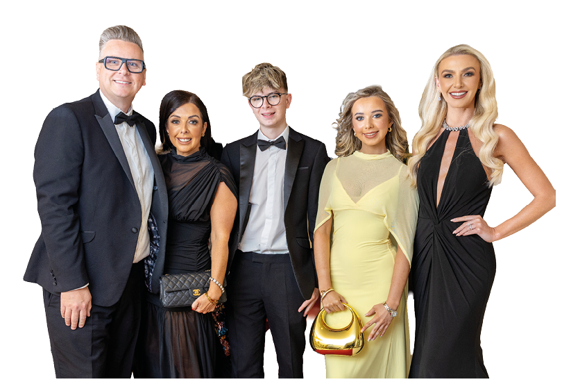 Five adults dressed in formal evening attire stand closely together smiling against a white background. Description generated by AI