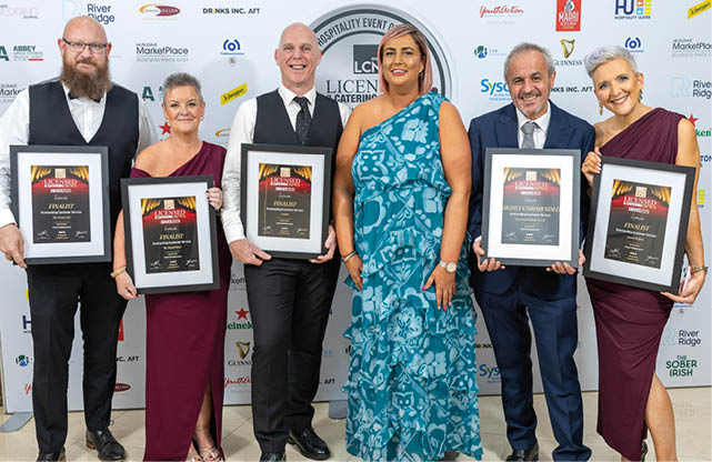 Five adults dressed in formal attire stand side by side holding framed awards against a backdrop with logos. Description generated by AI