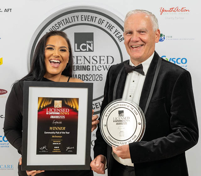 Two adults dressed formally are smiling and holding framed awards at a hospitality event. Description generated by AI