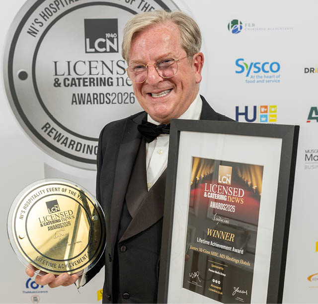 A person wearing glasses and a tuxedo is smiling and holding a framed award in front of a backdrop for the LCN License & Catering Awards 2026. Description generated by AI
