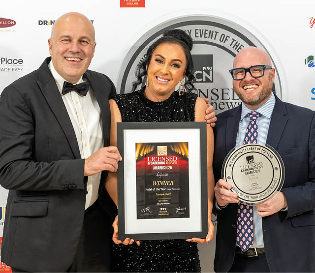 Three adults dressed in formal attire smile while holding an award plaque and a framed certificate at an event. Description generated by AI