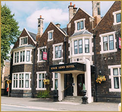 A historic stone building with multiple chimneys and bay windows displays a sign reading “Admir Arms Hotel" above the entrance, with flower baskets hanging on the exterior walls and a large tree nearby. Description generated by AI