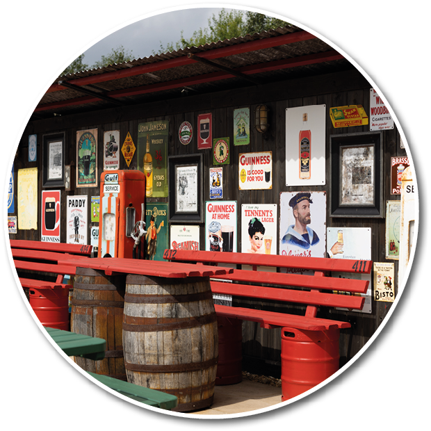 A vintage-style sign on a wooden wall advertises Guinness at home with an illustration of a smiling can and a glass of beer, accompanied by a smaller sign promoting Bird's Custard powder. Description generated by AI