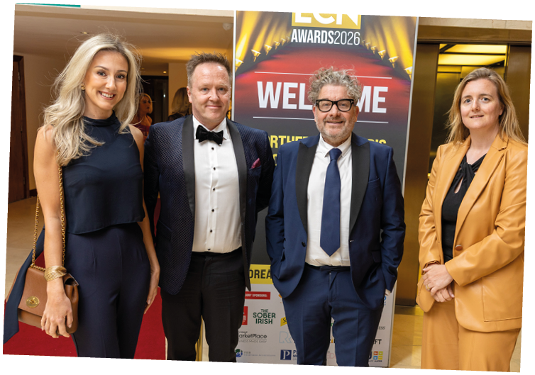 Four adults dressed in formal and business attire stand smiling in front of a welcome sign for an awards event. Description generated by AI
