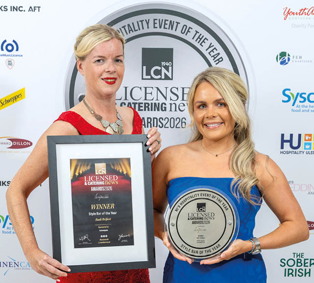 Two adults dressed in formal attire are smiling and holding an award plaque and a circular award at a Licensed Catering News event. Description generated by AI