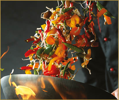 Closeup of chef throwing vegetable mix from wok pan in fire. Fresh asian food preparation on dark background.
