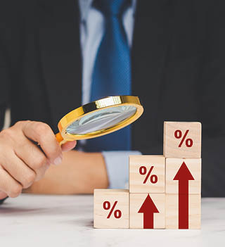 Interest rate financial concept. A Businessman is holding a magnifier and looking at wooden cubes with red arrows and percentage symbols on a wooden table.