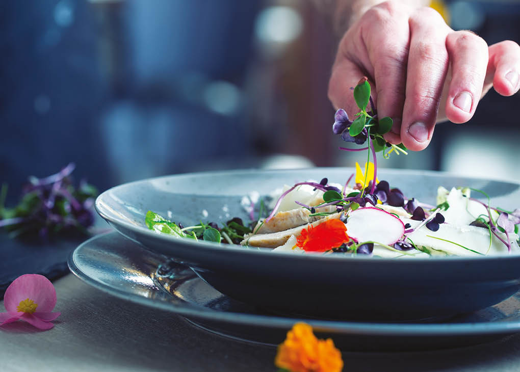Chefs hand prepares a salad with chicken meat and decorates this meal with herbs and edible flowers.