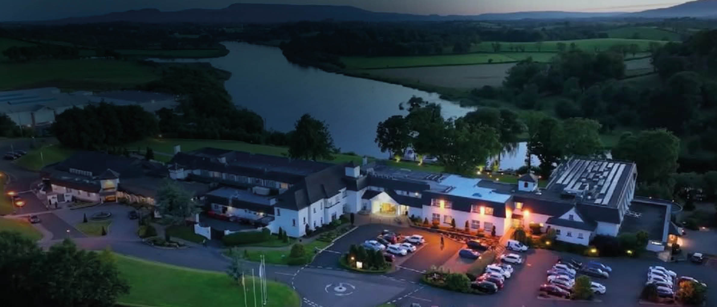 A large hotel with a parking lot and a lake in the background. Description generated by AI