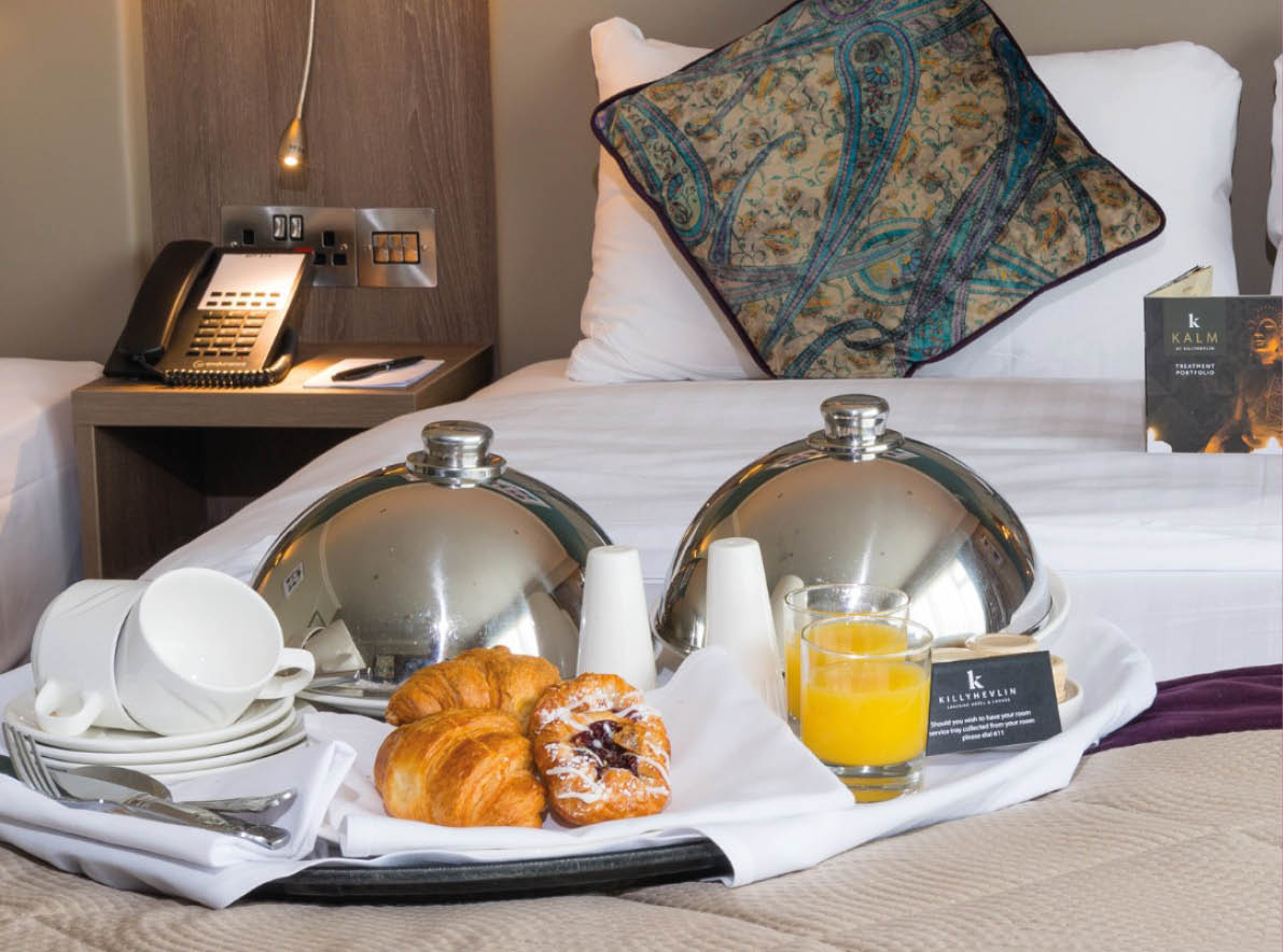 A bed with a tray of food and drinks on it. Description generated by AI