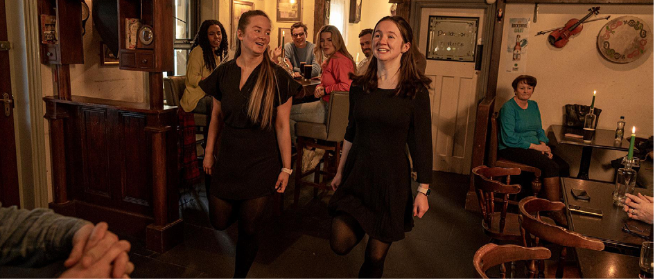 Two women in black dresses walking in a room. Description generated by AI