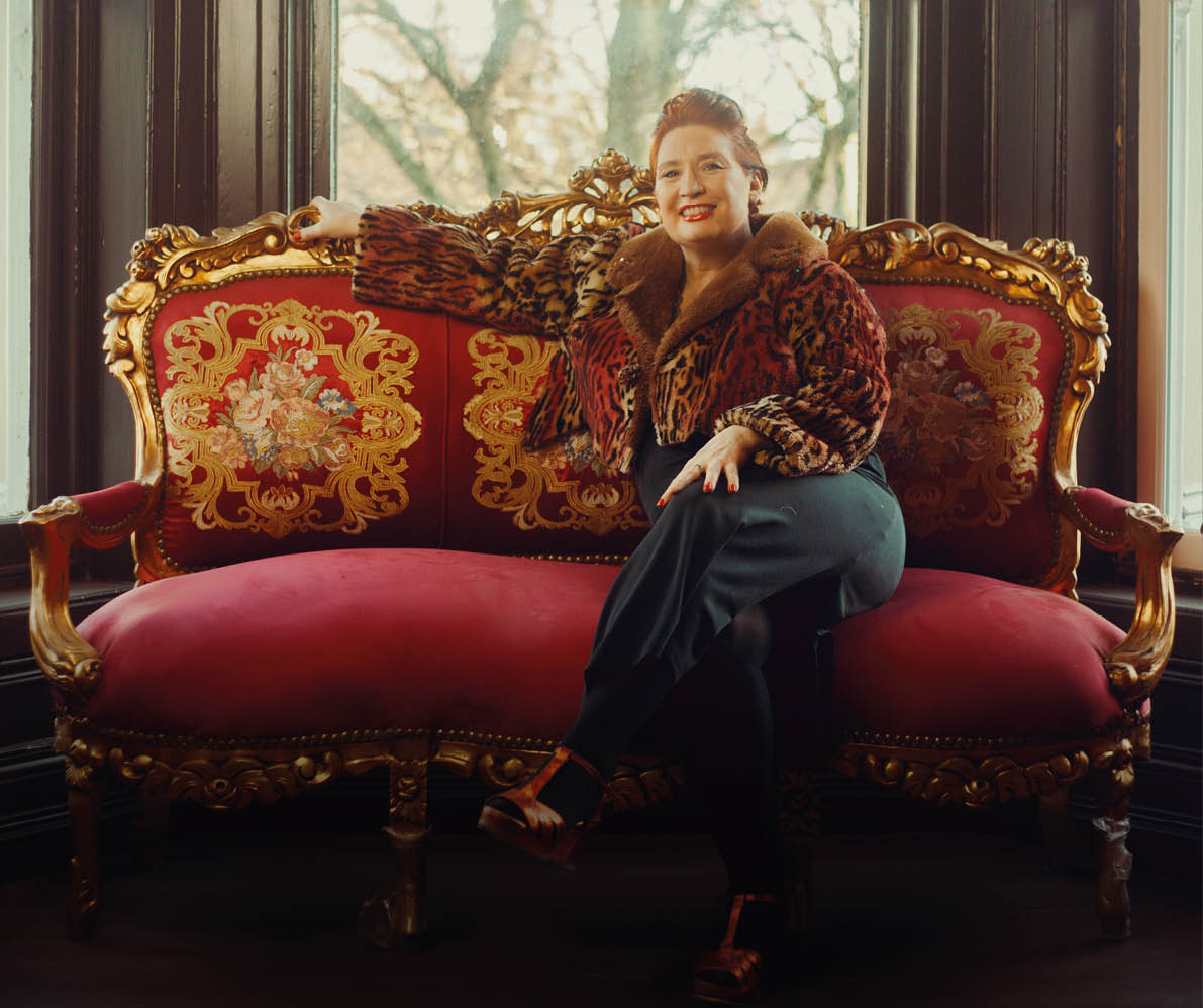 A woman is sitting on a red couch with a gold frame. Description generated by AI