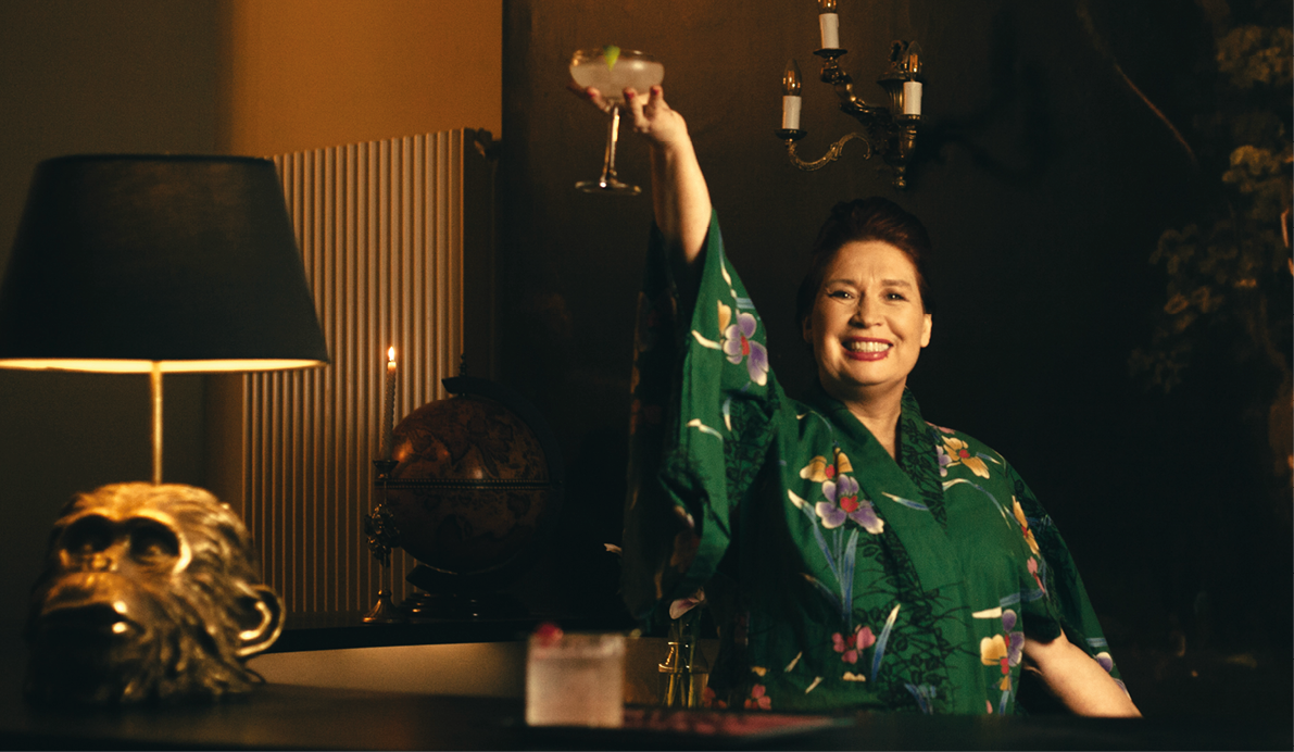A woman in a green dress is holding a glass of wine. Description generated by AI