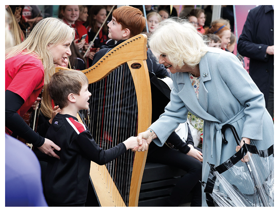 A woman in a blue coat shakes hands with a young boy. Description generated by AI