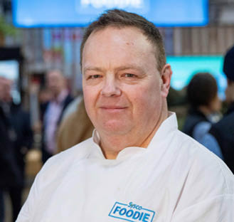 A man wearing a white shirt with the word Foodie on it. Description generated by AI