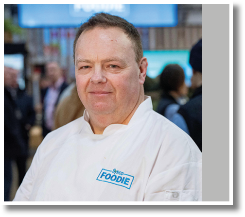A man wearing a white shirt with the word Foodie on it. Description generated by AI