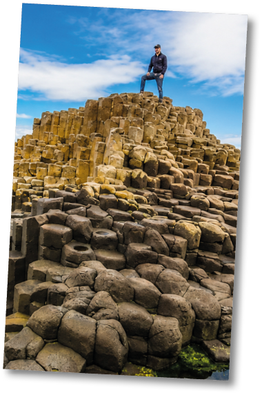 A man stands on a rock formation overlooking the ocean. Description generated by AI