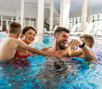 Smiling family of four having fun and relaxing in indoor swimming pool at hotel resort.
