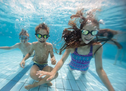 Little boys and a teenage girl are playing in resort swimming pool. They are smiling at the camera. Shot with a Nikon D850 DSLR camera, shallow depth of field.