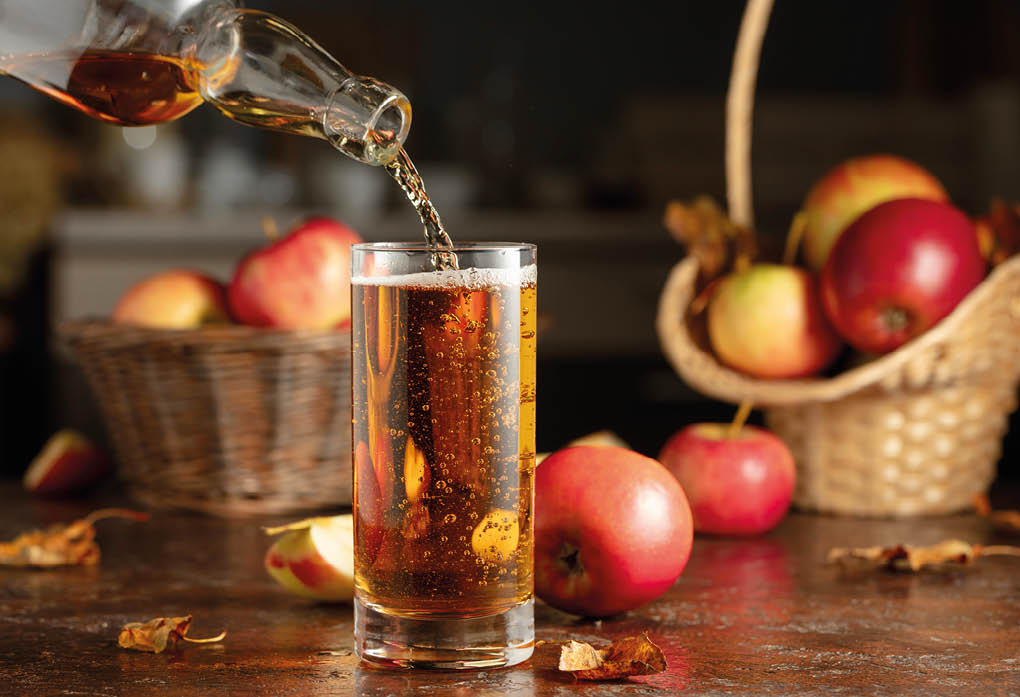 Apple cider is poured from a bottle into a glass. Fresh drink with apples on an old kitchen table.