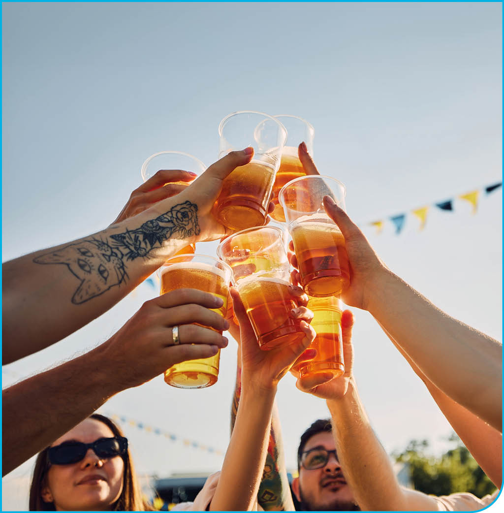 Group of people, friends gathering on picnic, raising glasses with beer, clinking under blue sunny clear sky. Traditional festival. Concept of summer, leisure, friendship, meeting, fun, relaxation