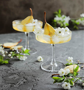 Pear cider in a beautiful wide glass with ice and dried pear pieces. Carbonated cocktail in glasses on a table with flowering twigs.