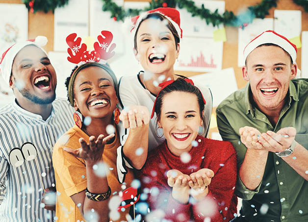 Christmas, office and business people blowing confetti and having fun together. Portrait, xmas party or group of happy employees, workers or coworkers celebrating with paper decorations in workplace