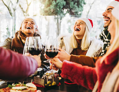 Happy family wearing santa claus hat having Christmas dinner party- Cheerful group of friends sitting at restaurant dining table celebrate xmas holiday cheering red wine glasses together