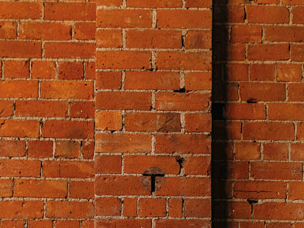 A close-up view of a red brick wall with a vertical column of bricks protruding slightly from the surface. Description generated by AI
