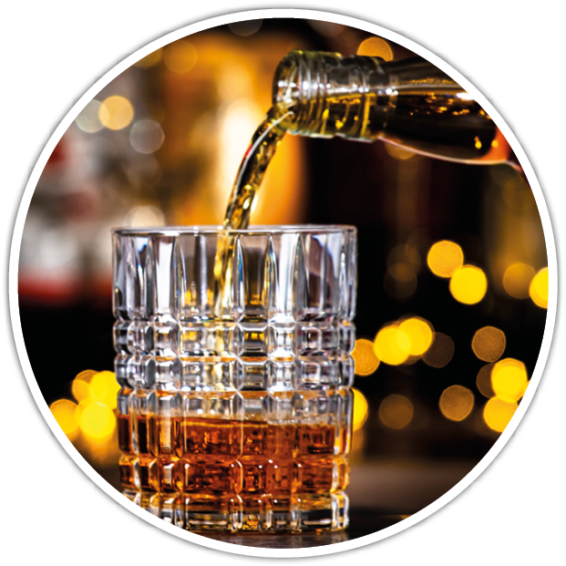 A glass with a textured pattern is being filled with a brown liquid from a bottle against a background of warm, blurred lights. Description generated by AI