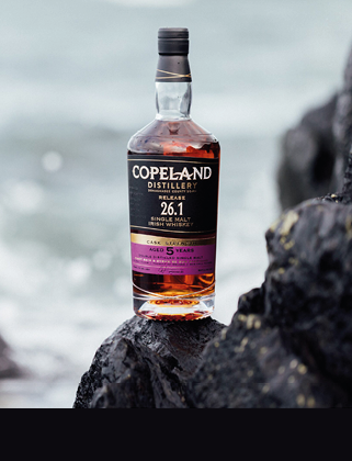 A bottle of Copeland Distillery single malt Irish whiskey aged 5 years is placed on a dark rock with a blurred ocean background. Description generated by AI