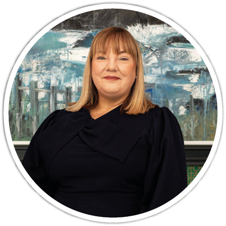 A person with straight shoulder-length hair wearing a dark outfit is smiling in front of an abstract blue and white painting. Description generated by AI