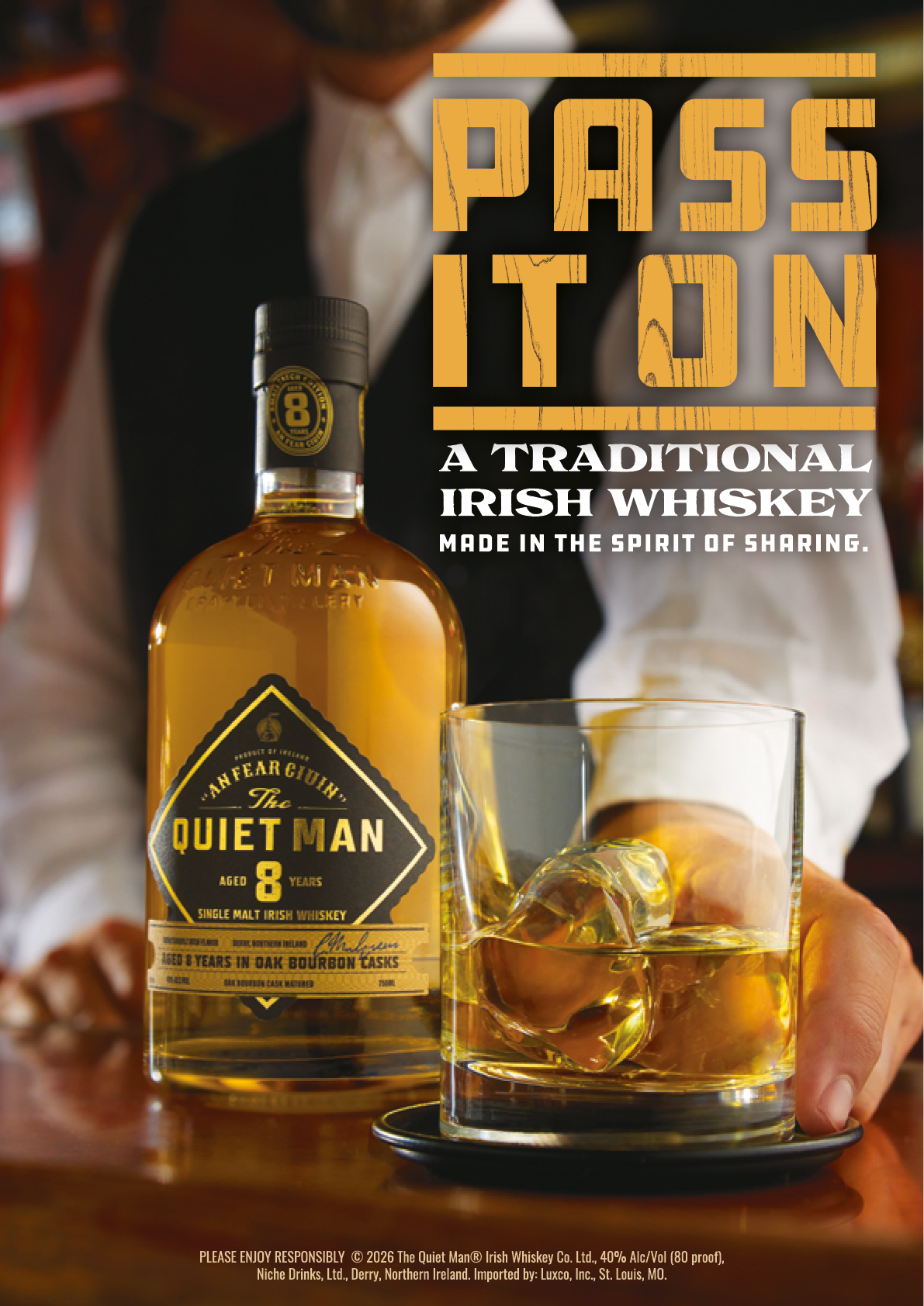 A person dressed in a white shirt and dark vest holds a glass of whiskey with ice next to a bottle of The Quiet Man Irish whiskey with the text “Pass It On A Traditional Irish Whiskey" above. Description generated by AI