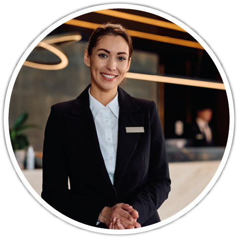 A person wearing a black suit and white shirt is smiling and standing with hands clasped in a modern indoor setting with warm lighting. Description generated by AI