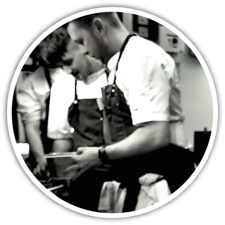 People wearing aprons are focused on preparing food in a kitchen setting. Description generated by AI