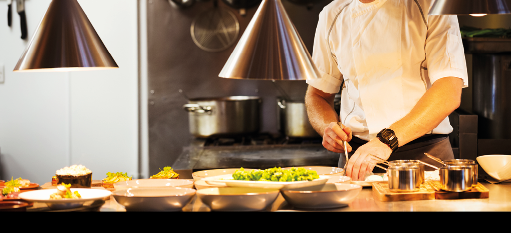 Chef standing in a restaurant kitchen, plating food.