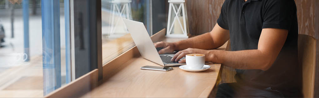 Handsome man working in cafe at window with coffee and laptop