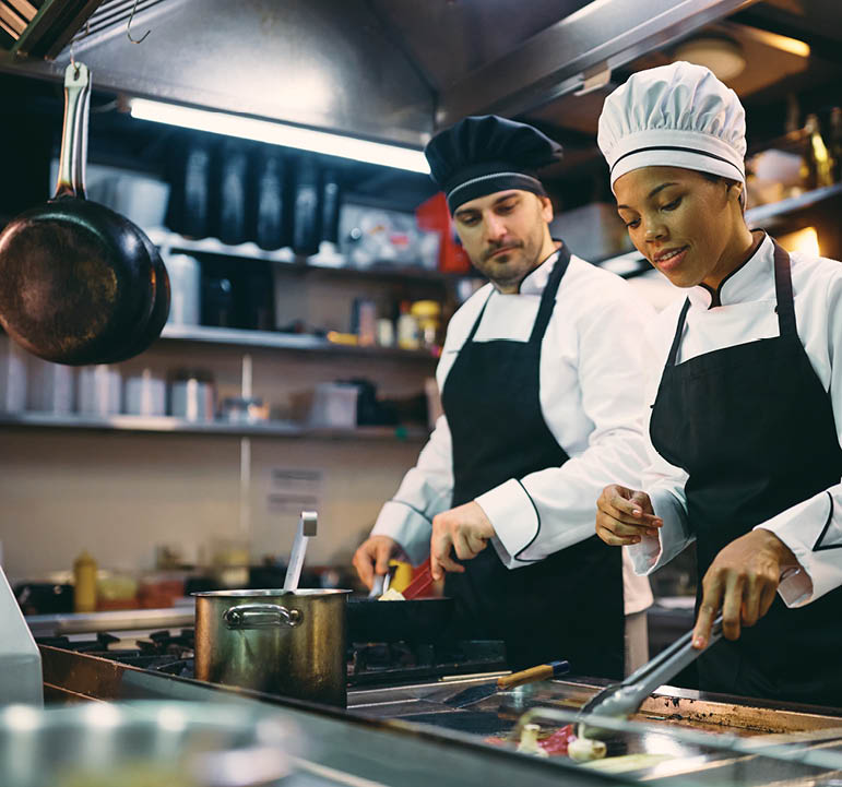 Two professional cooks preparing meal in the kitchen at restaurant. Focus is on African American female chef.