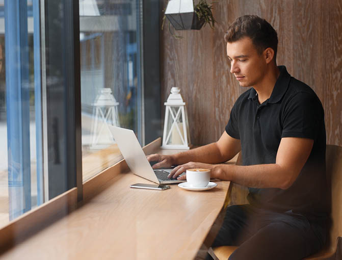 Handsome man working in cafe at window with coffee and laptop