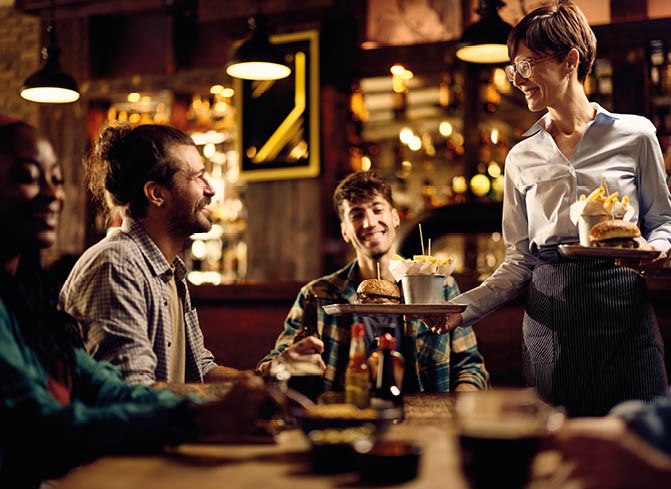 Happy waitress brining French fries and burgers to pub customers. 