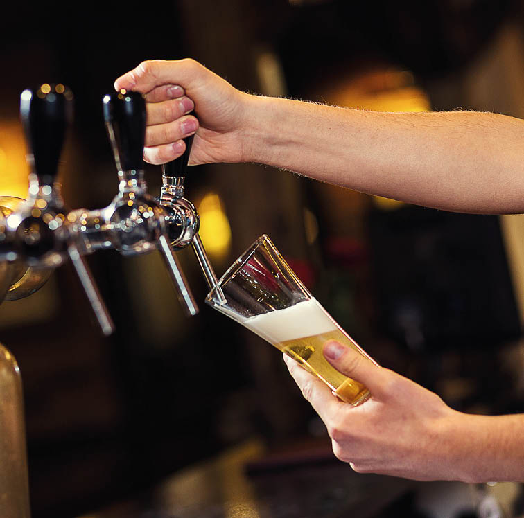 Bartender pouring from tap fresh beer into the glass in pub