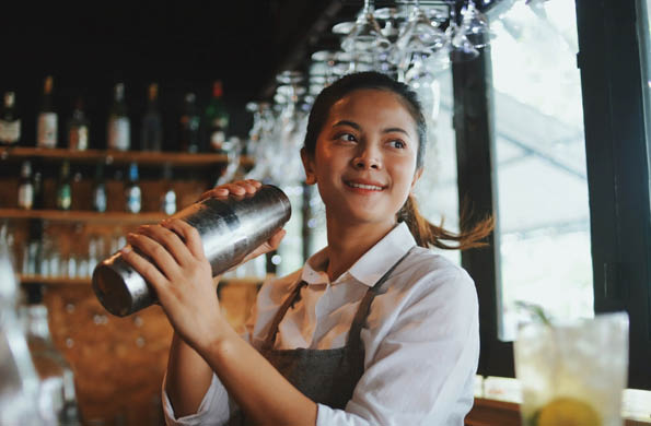 Beautiful Asian woman in gray apron preparing cocktail on the bar counter.