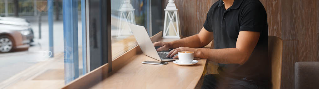 Handsome man working in cafe at window with coffee and laptop