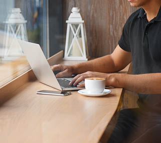 Handsome man working in cafe at window with coffee and laptop